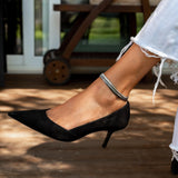 Silver snake chain anklet worn on an ankle with a pointed black heel, featuring a sleek, minimalist design.