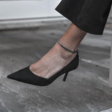 Silver snake chain anklet worn on an ankle, paired with a black high-heeled shoe, showcasing a sleek design.