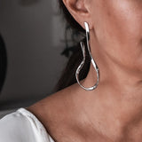 Large asymmetric dangle earrings feature textured hammered stud tops and flowing irregular wire dangles in a silver-tone finish.