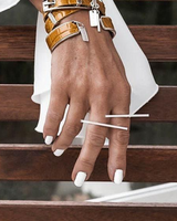 Geometric bar knuckle ring worn on a hand with white nails, showcasing an edgy, minimalist design against brown wood.