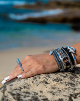 Geometric bar knuckle ring worn on a hand resting on a rock, complemented by stacked silver bracelets.