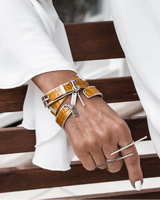 The geometric bar knuckle ring is worn on the index finger, featuring a sleek, elongated design in a shiny metallic finish.