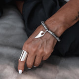 Stretchy silver hematite bracelet featuring a tooth charm, worn on a wrist, paired with a chunky silver ring.