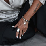 Silver hematite bracelet featuring a tooth charm, worn with a chunky silver ring and showcasing sleek, minimalist style.