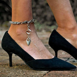 Stainless steel byzantine chain anklet with pendant, worn with a black high-heeled shoe, showcasing its shiny finish.