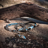 Solid square byzantine chain anklet features a stainless-steel design with a pendant and is shown resting on sand.