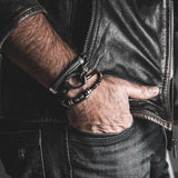 Black leather wrap bracelet with iron chains and metal elements, worn as a cuff on a man's wrist.