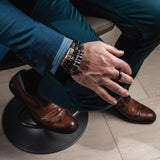 Men’s bracelet featuring silver-plated and leather elements on dark brown PU leather, worn with a suit and a chunky ring.