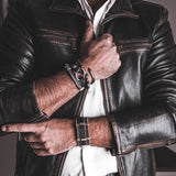 Black leather wrap bracelet with iron chains and metal elements, worn with adjustable buckle on wrist. Edgy unisex style.