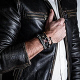 Unisex wrap bracelet with black leather, iron chains, and metal elements, worn on a wrist with a stylish leather jacket.
