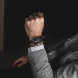 Men's labradorite beaded bracelet worn on wrist, layered with leather strap, features iridescent beads and minimalist style.