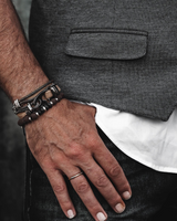 Hand wearing multiple bracelets and a ring, with a blurred background