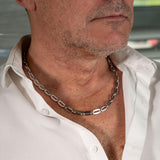 Casual minimalist stainless steel choker necklace on a man, featuring elongated oval links, styled with an unbuttoned white shirt.