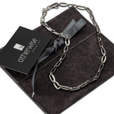 Minimalist men's necklace made of dark silver stainless steel links, presented on a suede pouch with a tag.