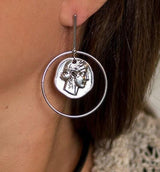 Contemporary statement earrings featuring a silver-toned Greek coin pendant in a circular design, worn on the ear.