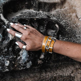 Wrap bracelet set in deep yellow leather with bold buckle, stacked with a matching moldable bangle. Silver rings adorn the hand.