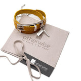 Yellow leather wrap bracelet with a bold buckle, accompanied by a silver plated metal bangle, on a suede pouch.