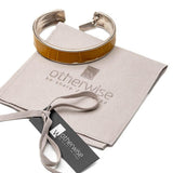 Yellow leather wrap bracelet with bold buckle paired with a silver antique-plated bangle, displayed on a suede pouch.