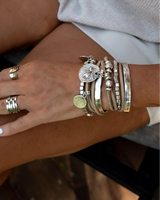Suede boho bracelet with coins and metal cubes, layered with silver-plated beads, worn on a wrist against a blurred background.