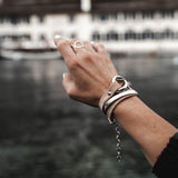 Silver-plated hammered bangle worn stacked with two leather bracelets on a hand with manicured nails.