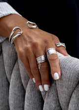 Unique hammered silver bangle with open cuff design, worn with stacking rings on a hand against a textured fabric background.