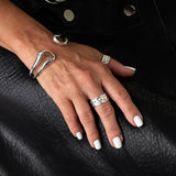 Unique hammered bangle in silver worn on the wrist, paired with other silver rings, against a black leather background.