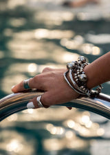 Bold hammered bangle bracelet stacked with other silver pieces, worn on a wrist gripping a metal railing by a pool.