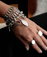 Unique hammered silver bangle worn stacked with multiple metal bracelets, showcasing a bold, edgy style.