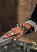 Silver hammered bangle layered with other bracelets on a wrist, featuring a coil design and adjustable fit.