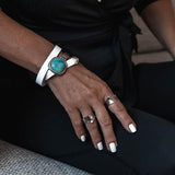 White leather wrap bracelet featuring a chunky turquoise resin stone and a half metal cuff, worn on a hand with silver rings.