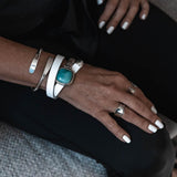 White leather wrap bracelet featuring a chunky turquoise resin stone and a half metal cuff, worn alongside silver bangles.