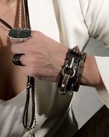 Leather statement bracelet features a silver-plated design with stitched leather and studs, worn stacked with other bracelets.