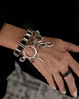 Hand wearing a silver bracelet with charms against a dark background