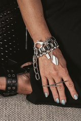 Person wearing black studded shoes and a black studded handbag, with silver jewelry on a textured surface.
