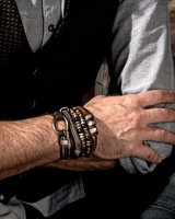Close-up of a person's arm with multiple bracelets and a ring, wearing a black vest and gray shirt.