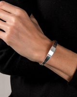 Silver-plated cuff bangle worn on a wrist, showcasing a geometric design with a smooth finish, adjustable for comfort.