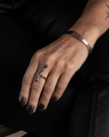 Silver-plated cuff bangle worn on a model's wrist, featuring a sleek, irregular shape, against a dark background.