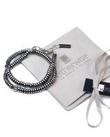 A beaded silver bracelet with a lobster clasp and branded tag, displayed next to a light gray velvet pouch and ribbon on a white background.