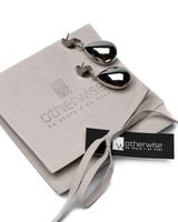 A pair of teardrop-shaped silver earrings with a polished mirror finish, presented on a light beige velvet pouch with a black 'otherwise' brand tag.