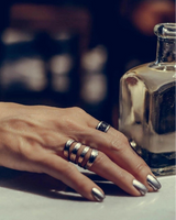 Funky hammered silver-plated metal ring worn on a hand with manicured nails, surrounded by multiple silver bangles.