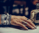 Funky hammered silver-plated metal ring worn on a hand with manicured nails, surrounded by multiple silver bangles.