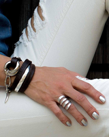 Chunky silver-plated hammered ring worn on a hand with metallic silver nails, alongside leather bracelets.
