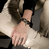 Chunky hammered silver-plated ring worn on a hand, paired with a braided leather and metal bracelet.
