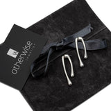 Minimal chic silver droplet earrings with an irregular shape, displayed on a black suede pouch.