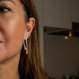 Modern geometric droplet earrings in silver, featuring a unique irregular shape, worn on the model's ear.