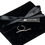 Adjustable stainless steel ring with a sleek, wavy design, displayed next to a black suede pouch with a ribbon.