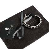 Antique silver bangle featuring black leather and silver studs, resting on a black suede pouch with a ribbon.