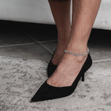 Dainty 999 silver antique plated anklet with charms, worn above a black high-heeled shoe on a tiled floor.