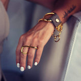 Funky two-finger ring in gold, featuring fluid curves and an adjustable geometric design on a hand with white nails.