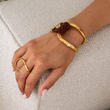 Adjustable irregular two-finger ring in gold, featuring fluid curves, worn on a hand alongside a brown leather bracelet.